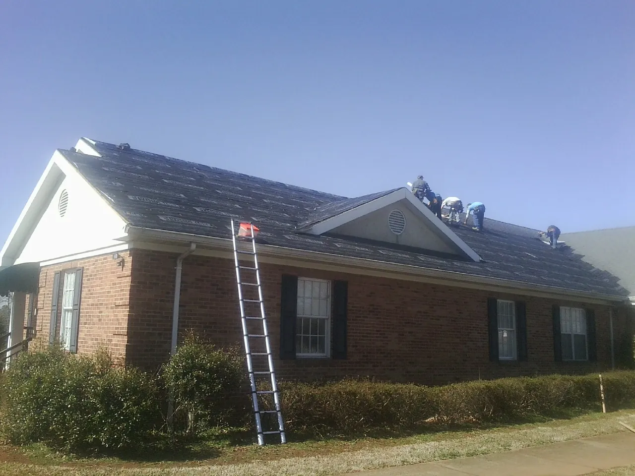 Crew tearing shingles off a brick ranch roof with a ladder set — Metal Roof Repair work by our crew in Putnam Valley