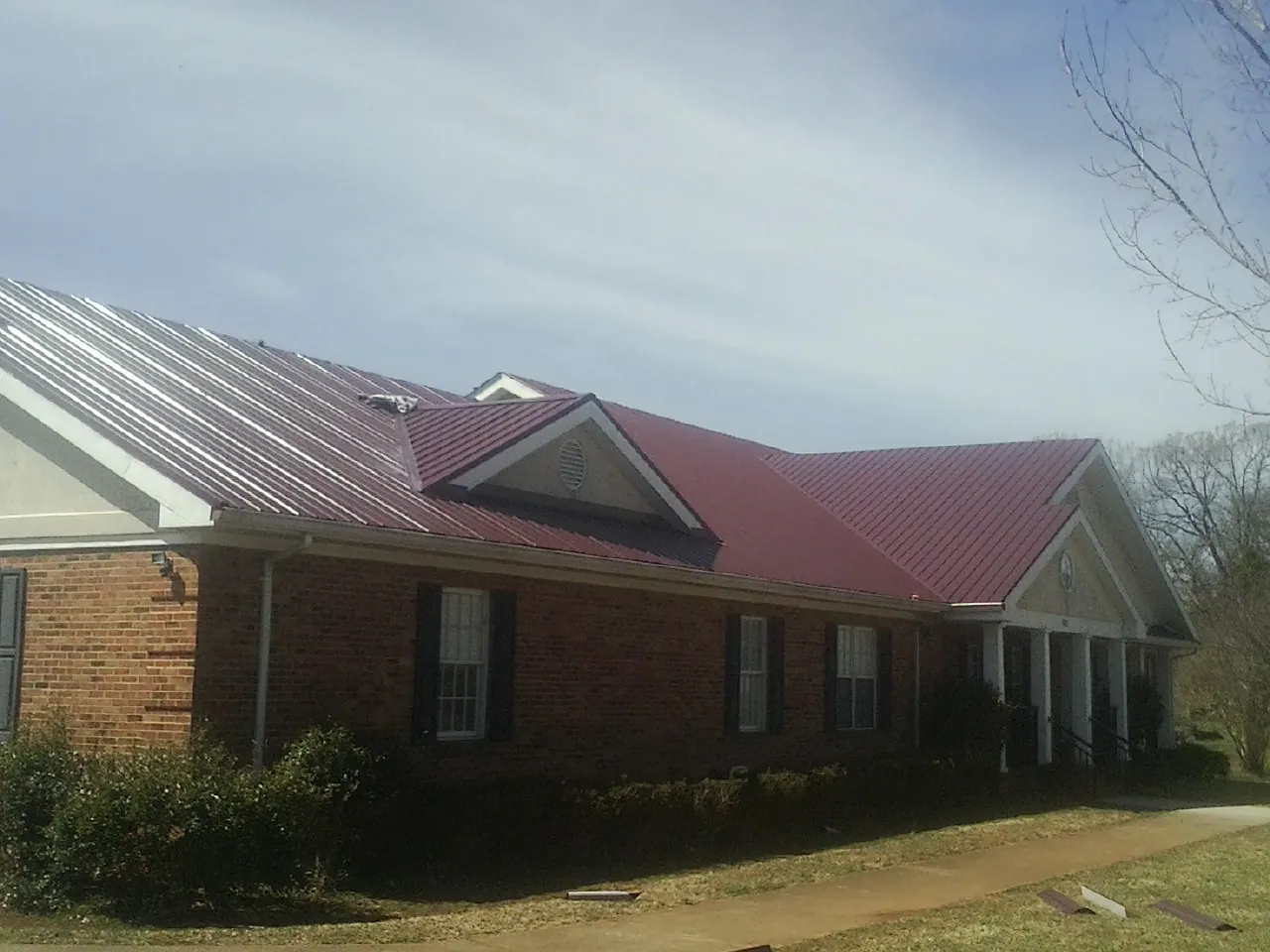 Red metal roof with gabled entries on a long brick building, from a Hail Damage Roof Repair job in Putnam Valley