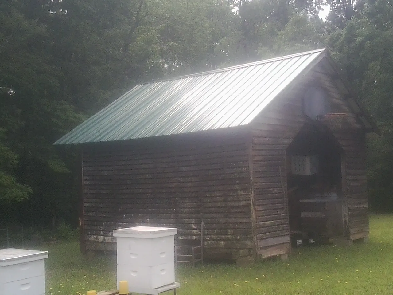 Green metal roof on a weathered barn beside stacked beehives in Putnam Valley