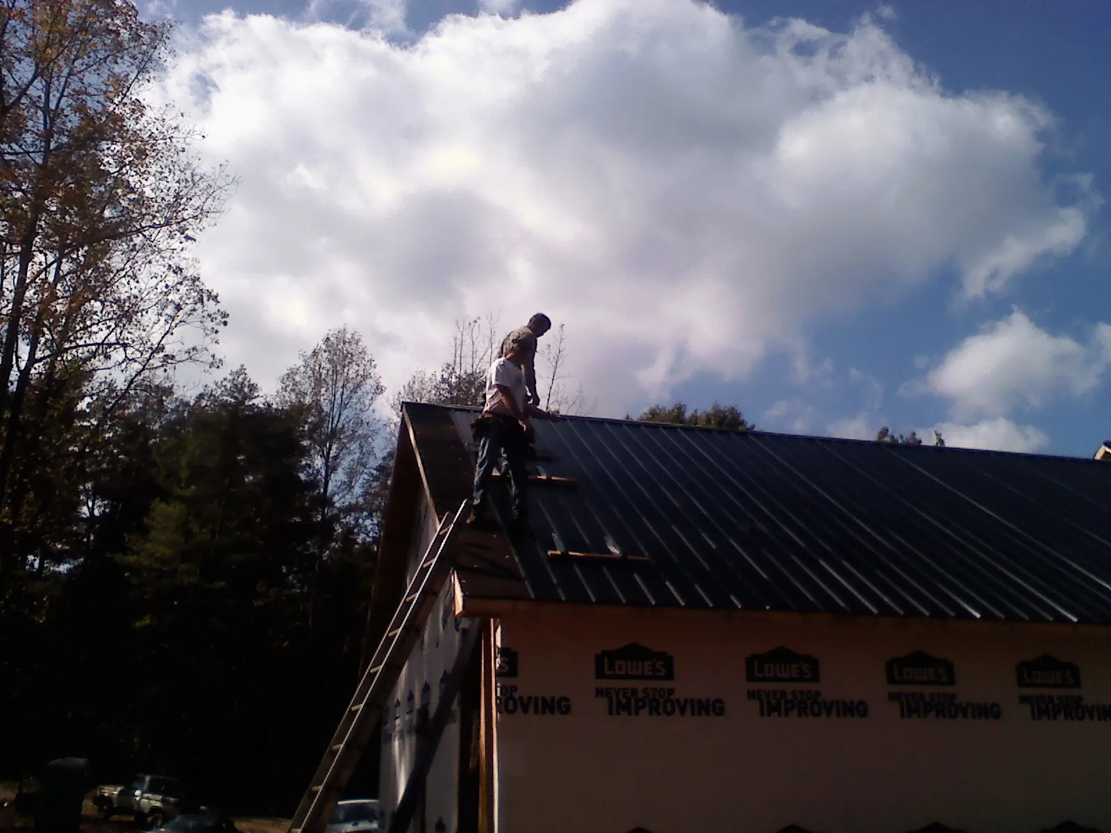 Roofer fastening dark metal panels high against a cloudy sky, from a Roof Inspection job in Putnam Valley