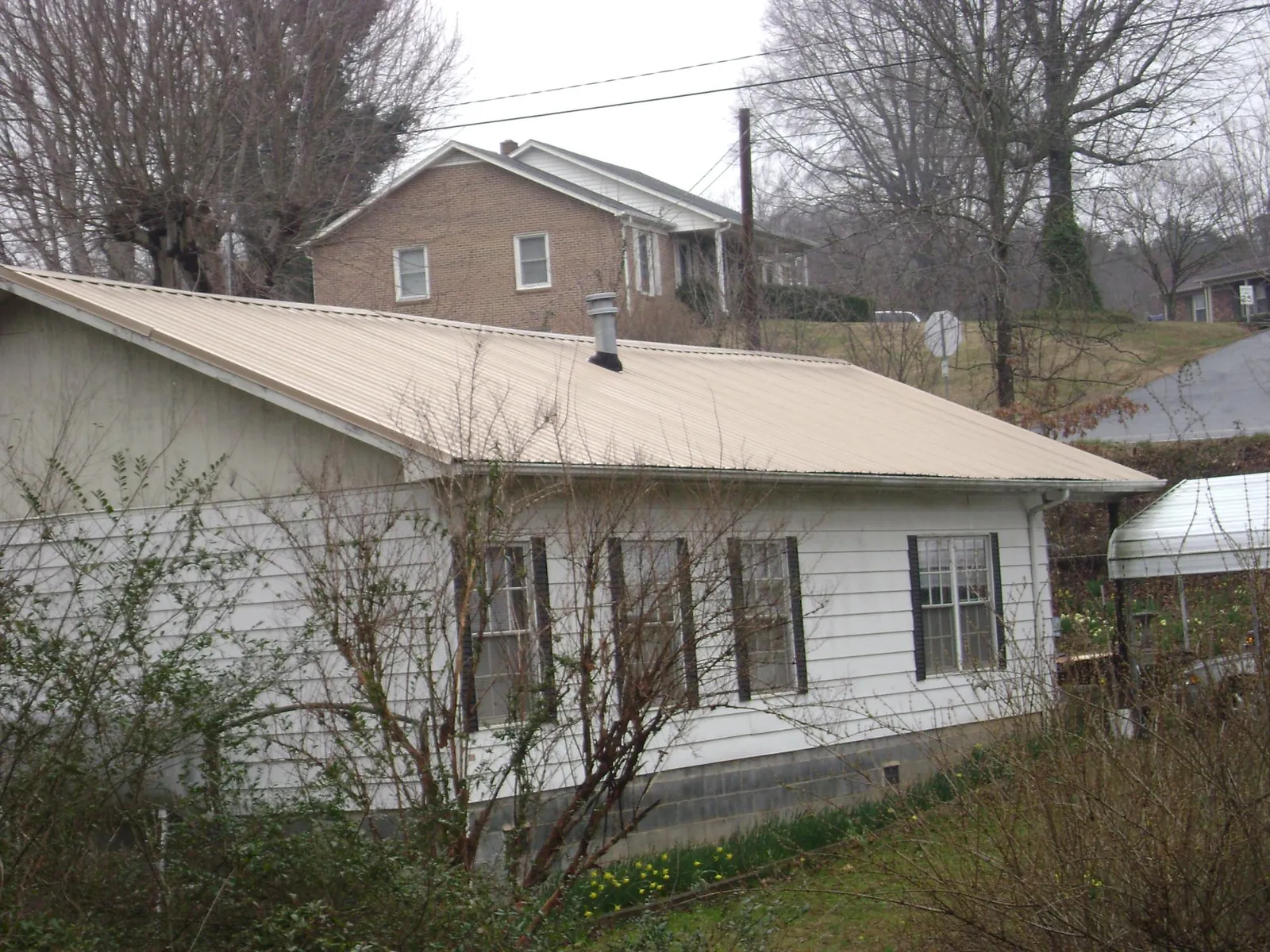 Tan metal roof on a white sided house set into a hillside — Commercial Roofing by Roofing Brothers in Putnam Valley